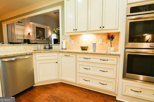 kitchen with light stone countertops, ornamental molding, appliances with stainless steel finishes, dark wood-style floors, and a sink