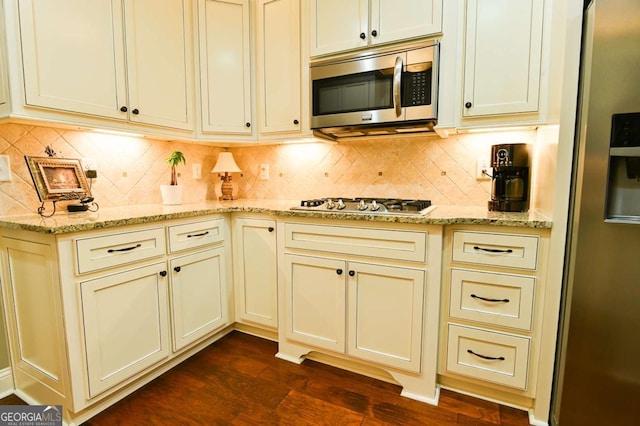 kitchen featuring light stone counters, cream cabinets, appliances with stainless steel finishes, decorative backsplash, and dark wood-style flooring