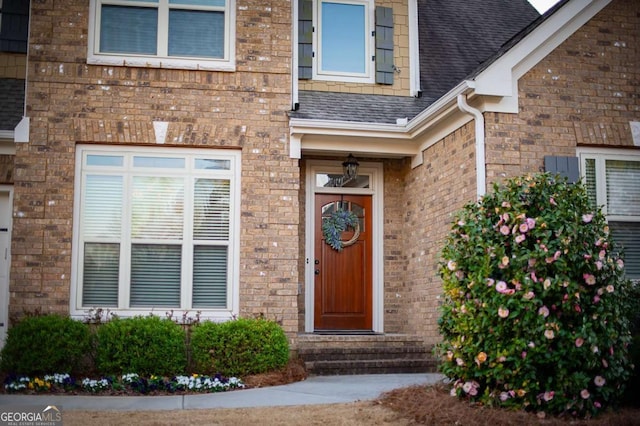 view of exterior entry with brick siding and roof with shingles