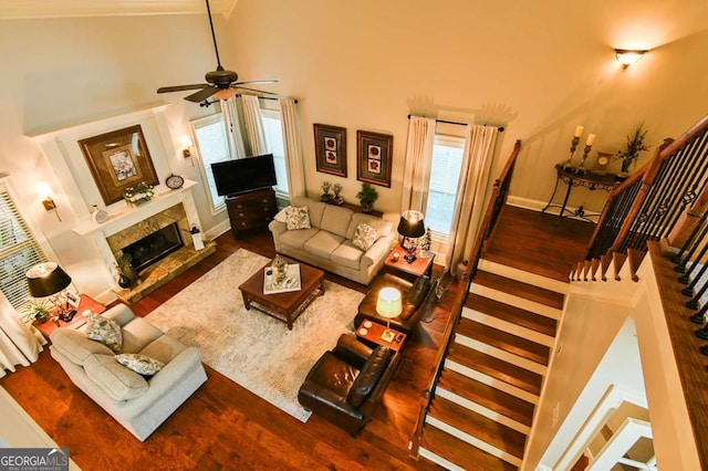 living area featuring a ceiling fan, wood finished floors, a high ceiling, a premium fireplace, and stairs