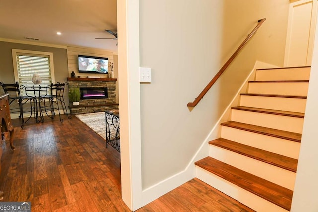 staircase featuring ceiling fan, baseboards, a stone fireplace, and wood finished floors