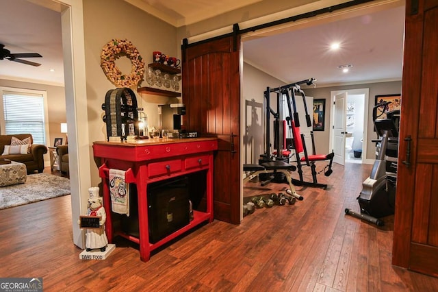 workout area featuring a barn door, ceiling fan, crown molding, and hardwood / wood-style flooring