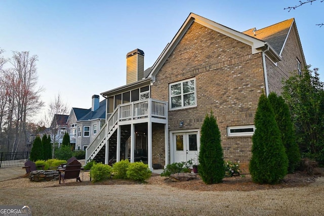 back of house featuring stairway, a sunroom, a chimney, a fire pit, and brick siding