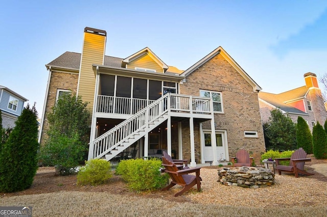 back of property featuring a sunroom, a chimney, stairs, a fire pit, and brick siding