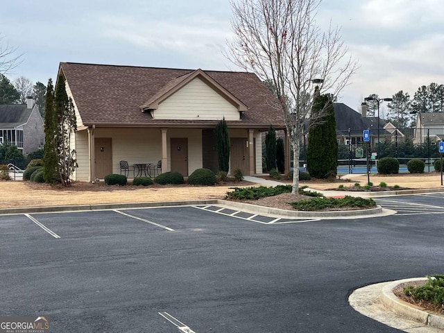 view of front of property featuring uncovered parking, fence, and a shingled roof