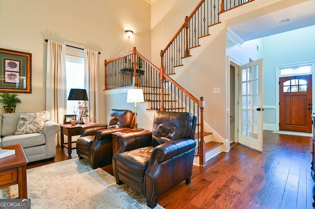 living area with a wealth of natural light, stairs, dark wood-type flooring, and a towering ceiling