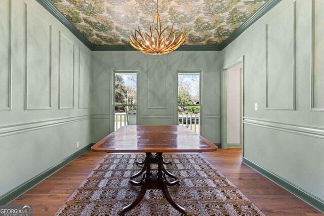 dining room with wood finished floors, an inviting chandelier, ornamental molding, and a decorative wall