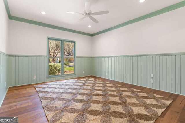 unfurnished room with crown molding, wood finished floors, a wainscoted wall, and ceiling fan