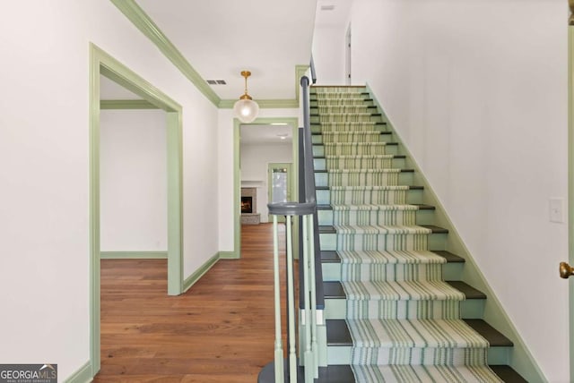 stairway with visible vents, ornamental molding, a warm lit fireplace, wood finished floors, and baseboards