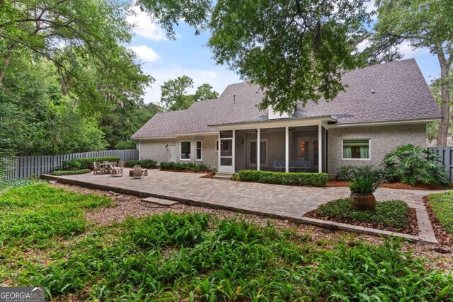 rear view of property featuring stucco siding, fence, a patio, and a sunroom