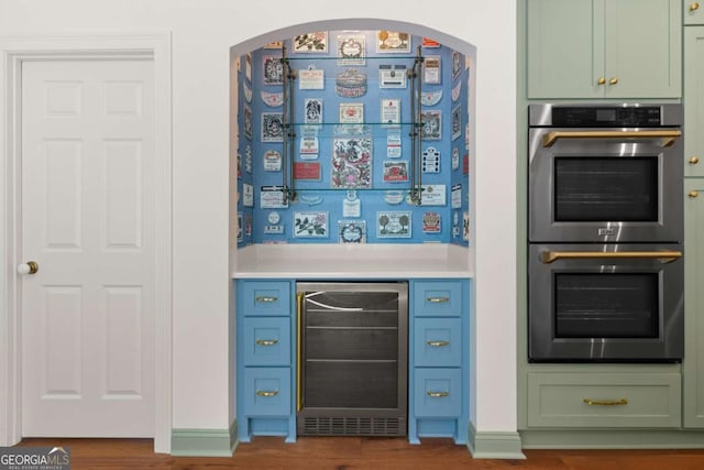 bar with wood finished floors, wine cooler, double oven, arched walkways, and a bar