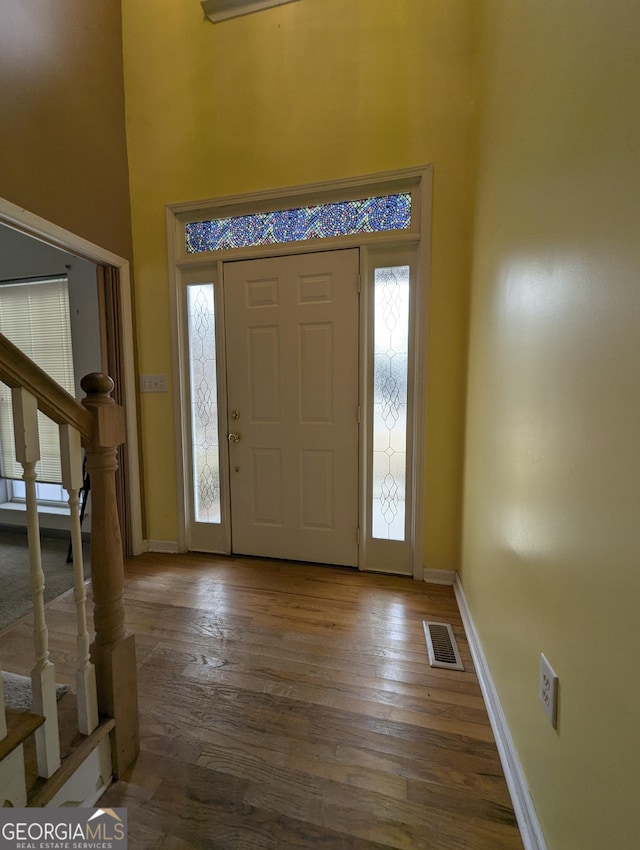 foyer entrance with visible vents, stairway, wood-type flooring, a high ceiling, and baseboards