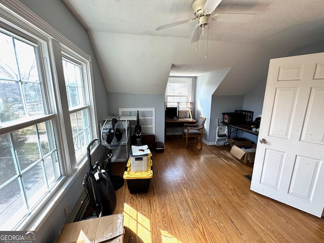 home office with a ceiling fan, wood finished floors, baseboards, vaulted ceiling, and a textured ceiling