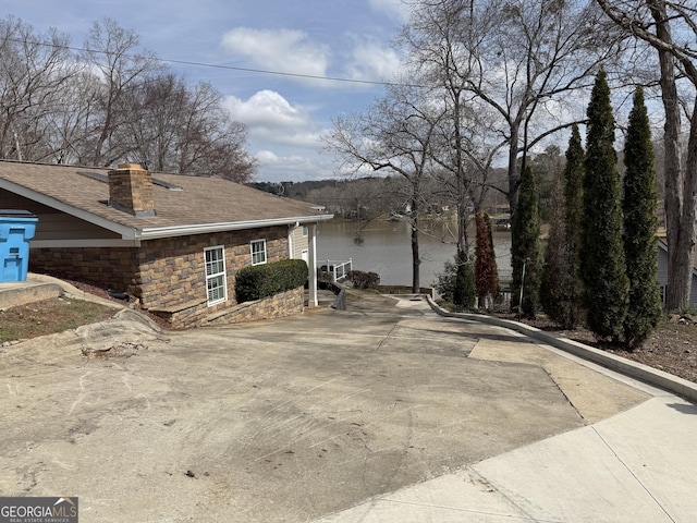 view of side of home with stone siding, a chimney, and roof with shingles