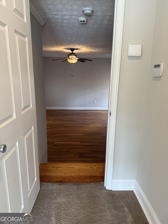 hallway featuring baseboards, a textured ceiling, and carpet floors