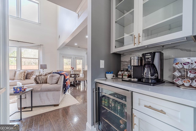 kitchen with beverage cooler, dark wood finished floors, light countertops, glass insert cabinets, and backsplash