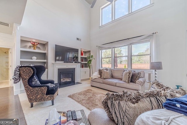 living area featuring built in features, a fireplace with flush hearth, and visible vents