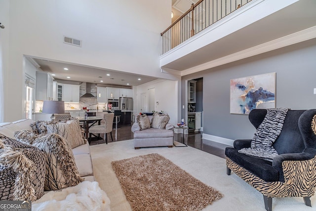 living area with visible vents, a high ceiling, baseboards, and ornamental molding