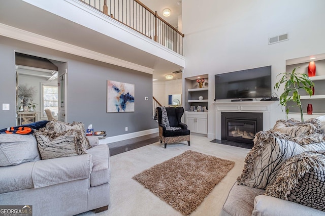 living room featuring visible vents, a fireplace with flush hearth, built in features, crown molding, and baseboards