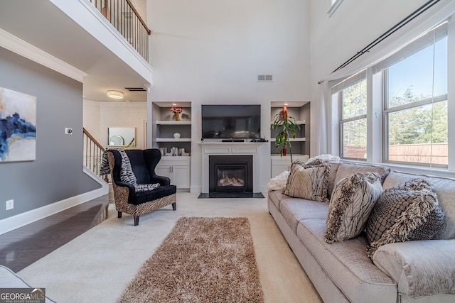 living room with visible vents, built in shelves, baseboards, a fireplace with flush hearth, and stairs