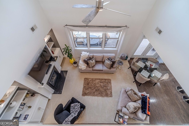 living area featuring visible vents, wood finished floors, a high ceiling, and ceiling fan