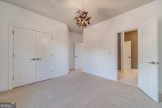 unfurnished bedroom with baseboards, light colored carpet, a closet, and a chandelier