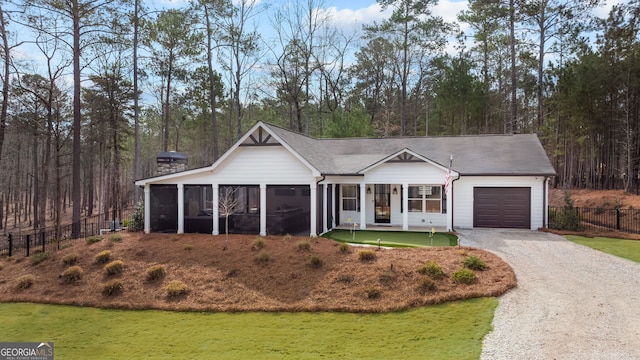 view of front of property with fence, gravel driveway, an attached garage, a sunroom, and a front lawn