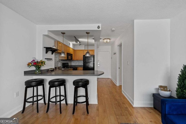 kitchen with light wood-style flooring, a peninsula, black appliances, and a breakfast bar area