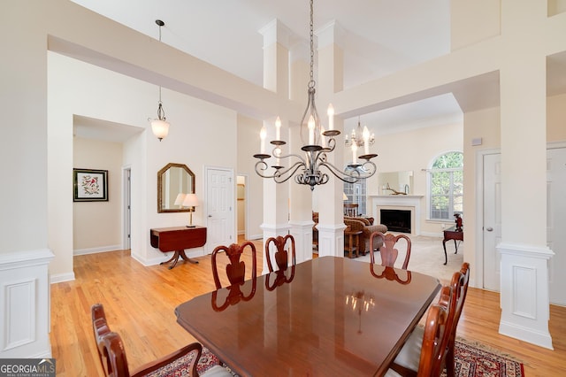 dining room featuring baseboards, a high ceiling, a fireplace, light wood-type flooring, and a chandelier