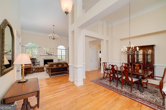 dining room featuring a wainscoted wall, light wood-type flooring, ornamental molding, a fireplace, and a notable chandelier