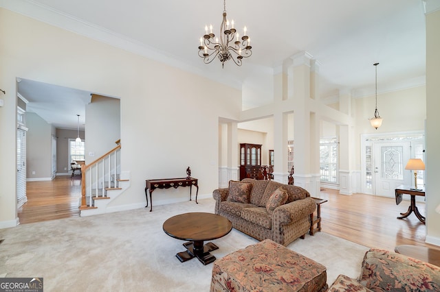 living room featuring light carpet, a notable chandelier, ornamental molding, stairway, and a towering ceiling