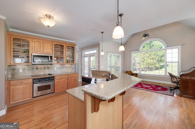 kitchen featuring a breakfast bar, decorative backsplash, appliances with stainless steel finishes, light wood-style floors, and a sink