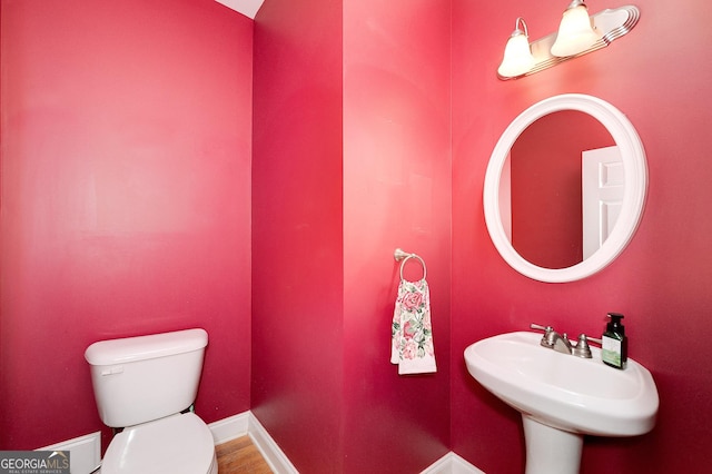 half bathroom with a sink, baseboards, toilet, and wood finished floors