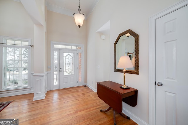 foyer with light wood finished floors, crown molding, a high ceiling, and decorative columns