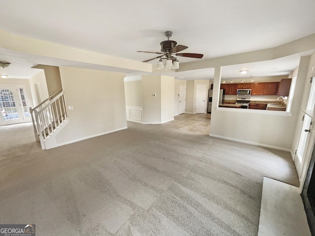 unfurnished living room with light carpet, stairs, a ceiling fan, and a sink