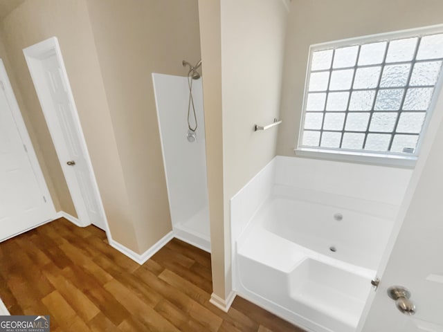 bathroom featuring a garden tub, walk in shower, and wood finished floors