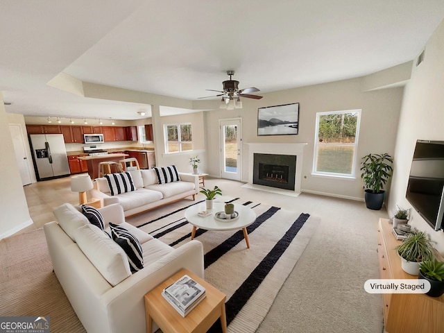 living room featuring a fireplace with flush hearth, light carpet, plenty of natural light, and a ceiling fan