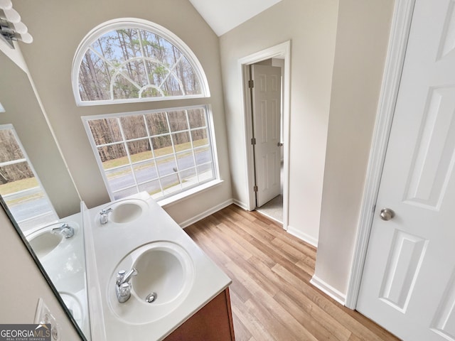 full bath with wood finished floors, baseboards, double vanity, lofted ceiling, and a sink