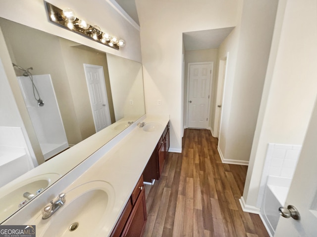 bathroom featuring wood finished floors, baseboards, double vanity, a sink, and a garden tub