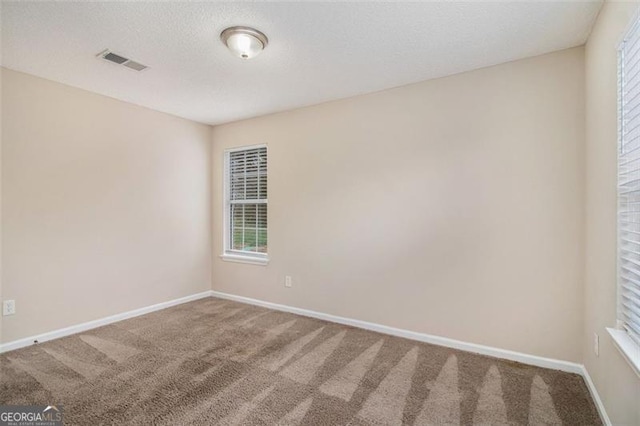 empty room with carpet flooring, baseboards, visible vents, and a textured ceiling