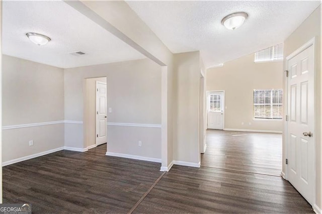 empty room featuring visible vents, baseboards, dark wood-type flooring, and a textured ceiling