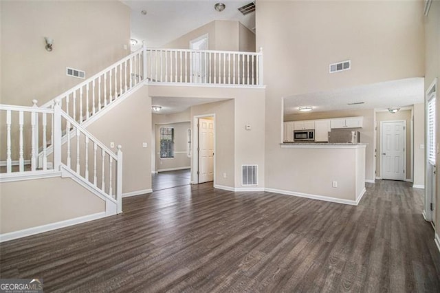 unfurnished living room with dark wood-type flooring, stairway, and visible vents