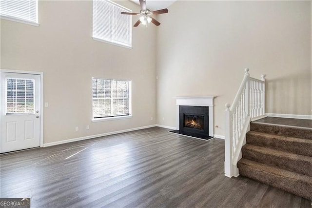 unfurnished living room featuring dark wood finished floors, a glass covered fireplace, a healthy amount of sunlight, and ceiling fan