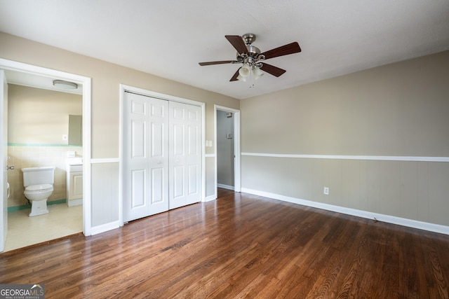 unfurnished bedroom featuring a wainscoted wall, a ceiling fan, wood finished floors, connected bathroom, and a closet