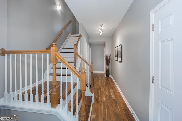 stairs featuring baseboards, wood finished floors, and track lighting