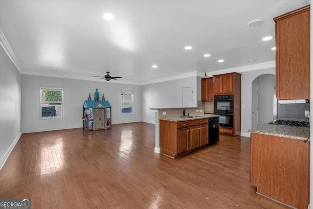 kitchen with dobule oven black, brown cabinets, wood finished floors, arched walkways, and a ceiling fan