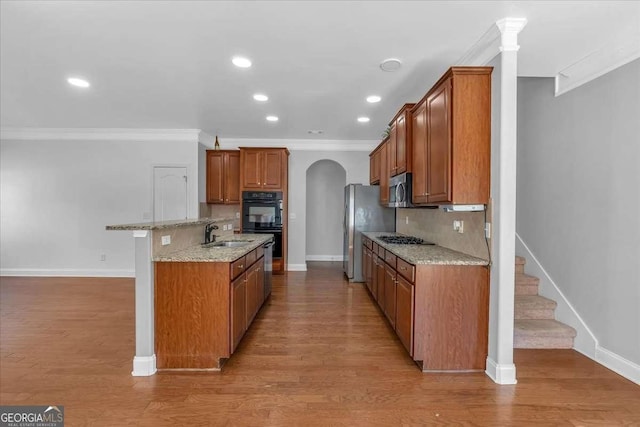 kitchen featuring brown cabinets, a sink, arched walkways, appliances with stainless steel finishes, and decorative backsplash