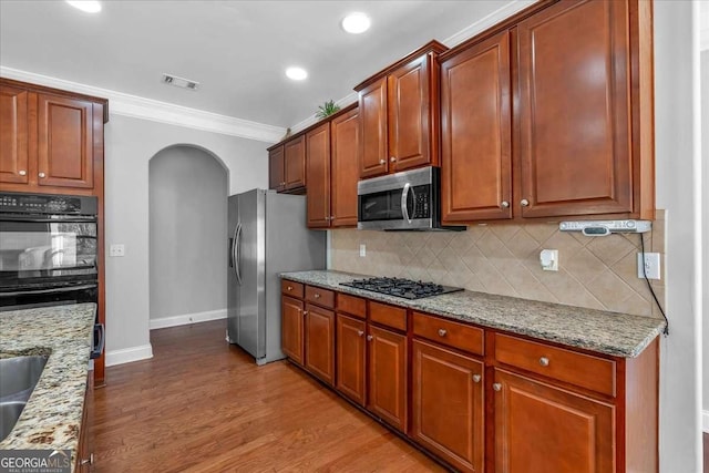 kitchen with visible vents, black appliances, ornamental molding, arched walkways, and light wood finished floors