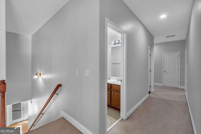 hallway featuring a sink, visible vents, an upstairs landing, and baseboards