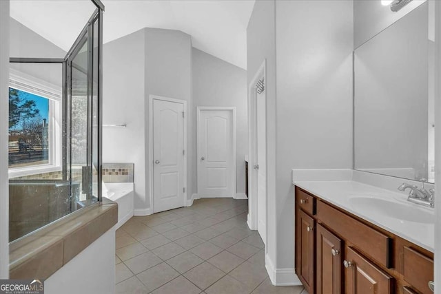 full bath featuring tile patterned floors, a garden tub, lofted ceiling, baseboards, and vanity